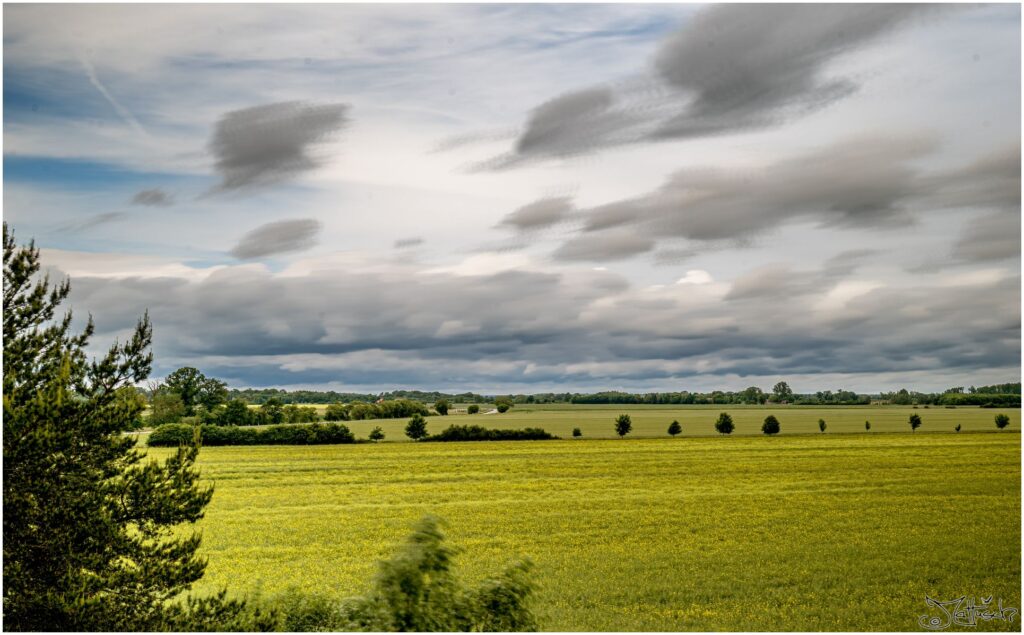 Ein Blick über gelbe Rapsfelder und Wolkenhimmel von erhöhter Position. Langzeitbelichtung.